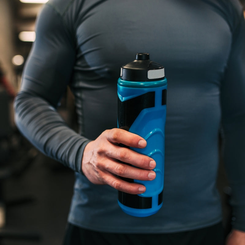 A close-up of a person in a gym holding a blue and black athletic water bottle.